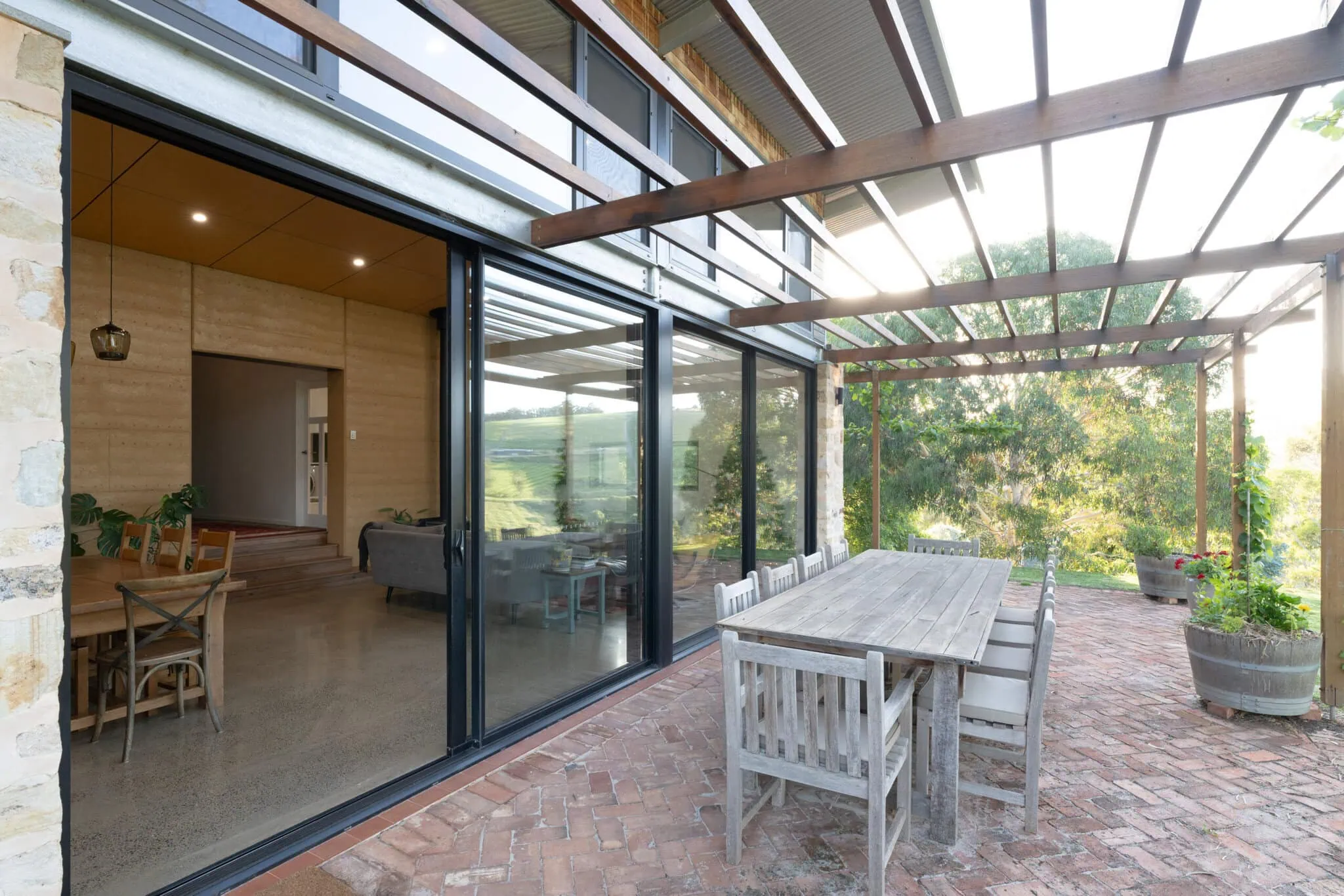 Bright outdoor deck with glass doors, brick flooring, and timber pergola.