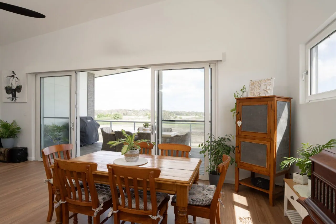 Indoor dining space with large sliding glass doors leading to balcony, filled with natural sunlight and greenery.