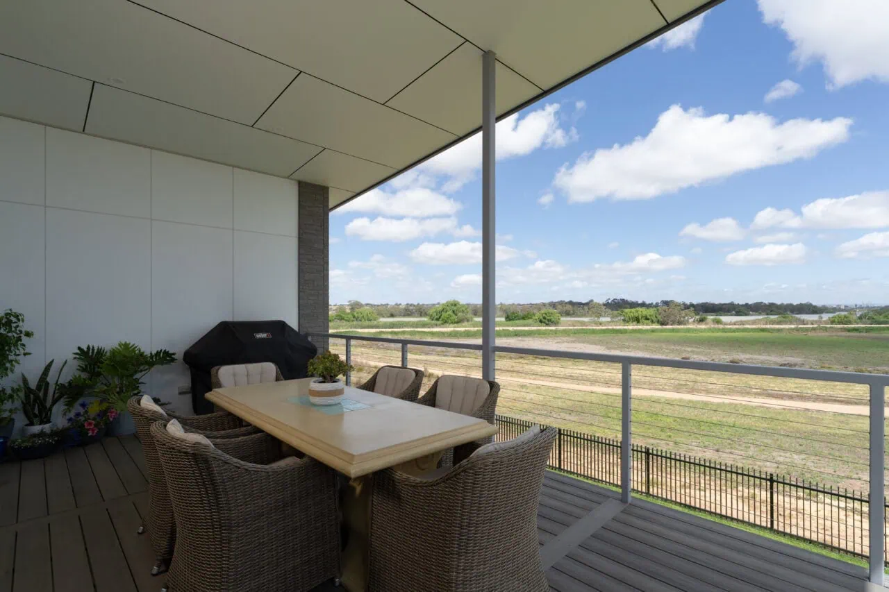 Stylish outdoor balcony with seating, overlooking lush farmland under blue sky.