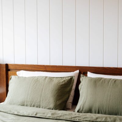 Comfortable bedroom with green linen bedding and wooden headboard, showcasing stylish and cozy inter.