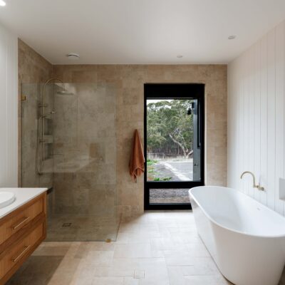 Bathroom with freestanding bathtub and walk-in shower, featuring natural stone tiles and contemporar.