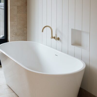 Freestanding bathtub with gold faucet in contemporary bathroom setting.