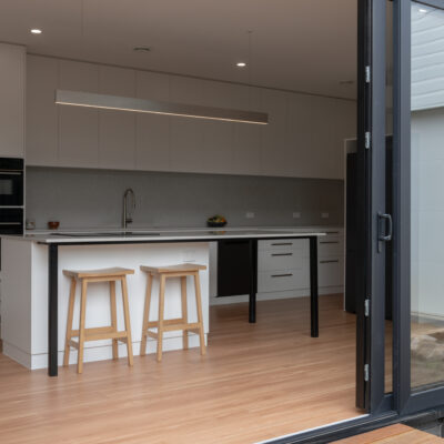 Contemporary kitchen with white cabinets and wooden stools at Project West Beach.