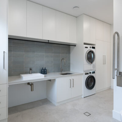 Contemporary laundry room with white cabinetry and washer-dryer units.