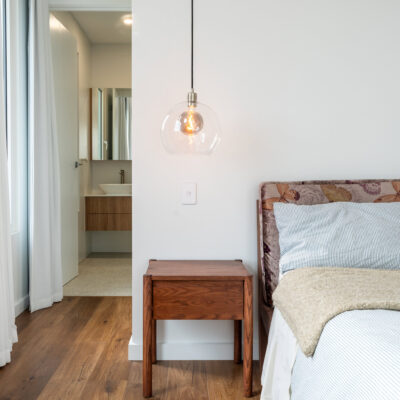 Contemporary bedroom with wooden side table and pendant light.