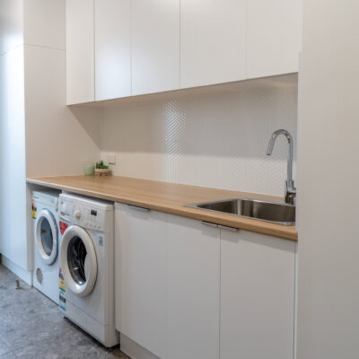 Contemporary laundry room with white cabinetry and wooden benchtop.
