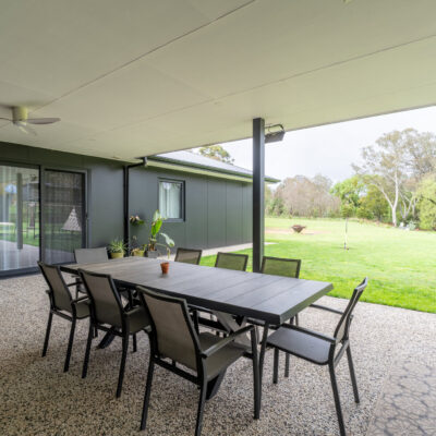 Covered outdoor patio with dining table and chairs overlooking green yard.