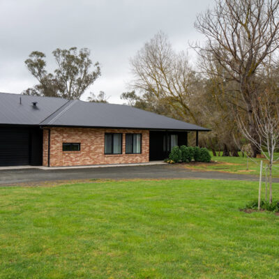 Contemporary brick house with a dark roof and lush green lawn in a suburban setting.