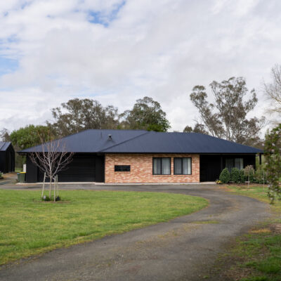 Contemporary single-story house with black roof and brick facade in a lush yard.